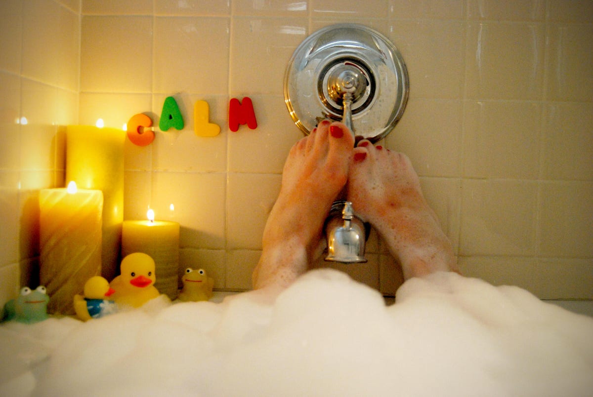A woman relaxes in a bubble bath, feet up. There are candles and letters that spell out 