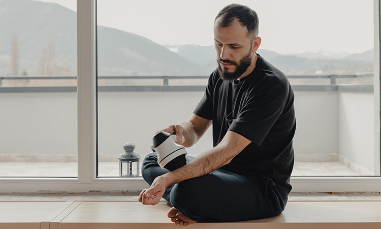 An image of a man applying percussion massage to his arm muscles with a massage gun is used to illustrate the concept of a wellness program.