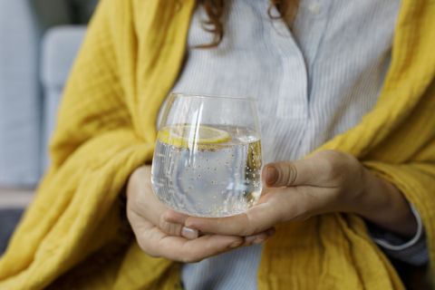 hands of woman holding sparkling water with lemon slice in glass