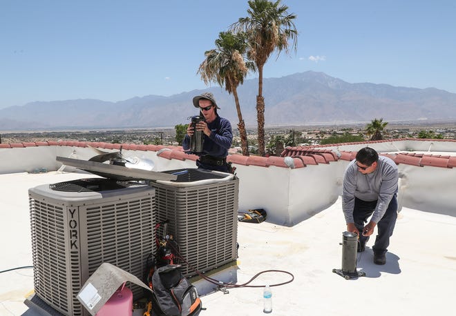 Van Tallian, left, and Erik Smith replace a compressor on a broken air conditioner at an apartment complex in Desert Hot Springs, June 9, 2022.  The two were working in the triple-digit temperatures for Direct AC.