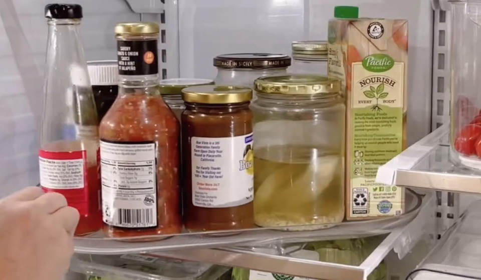 someone turning the lazy susan filled with jars and condiments in a fridge